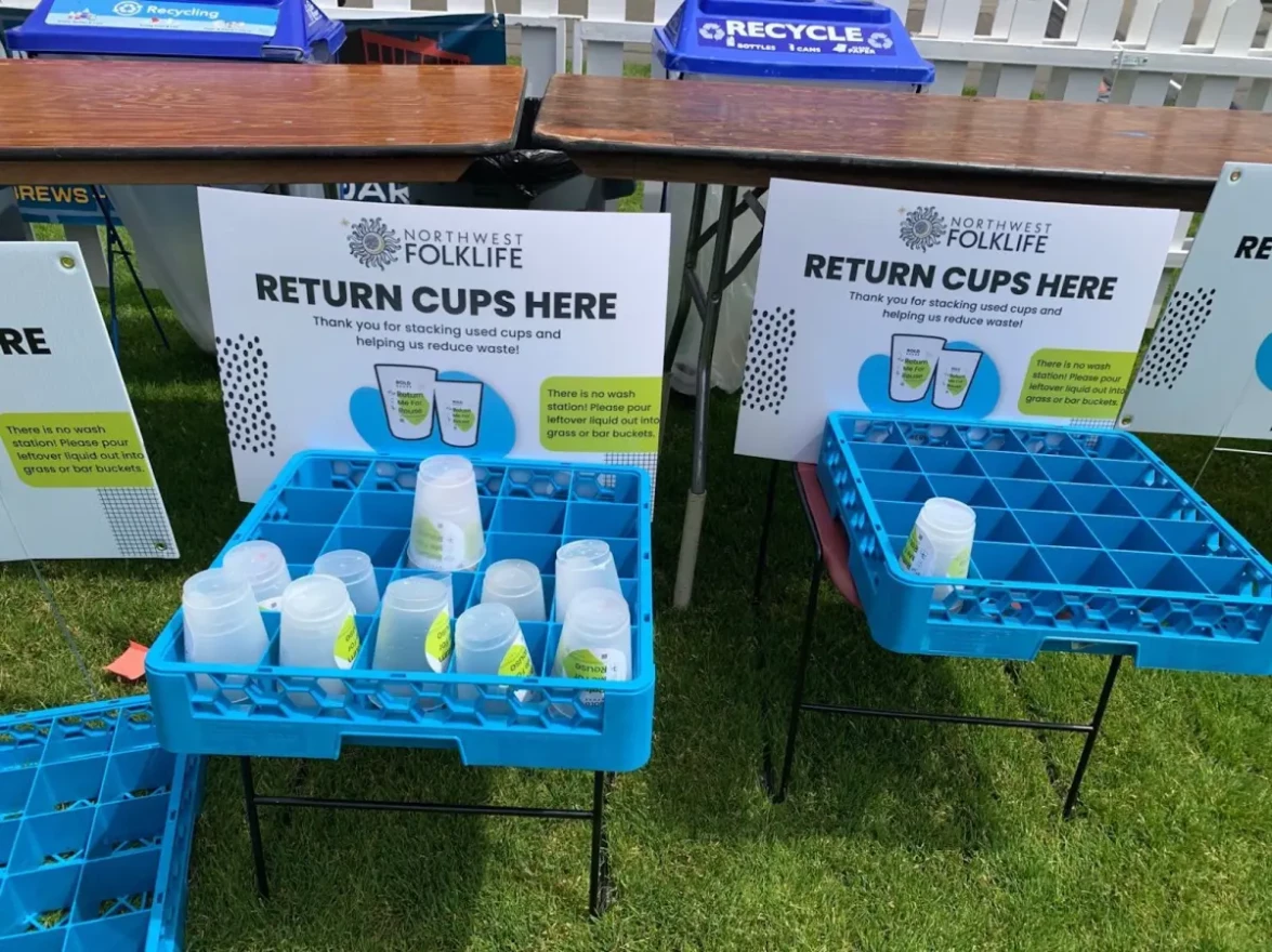 Crates with cups stacked inside of them sit on chairs with signs above them reading, "Return cups here."